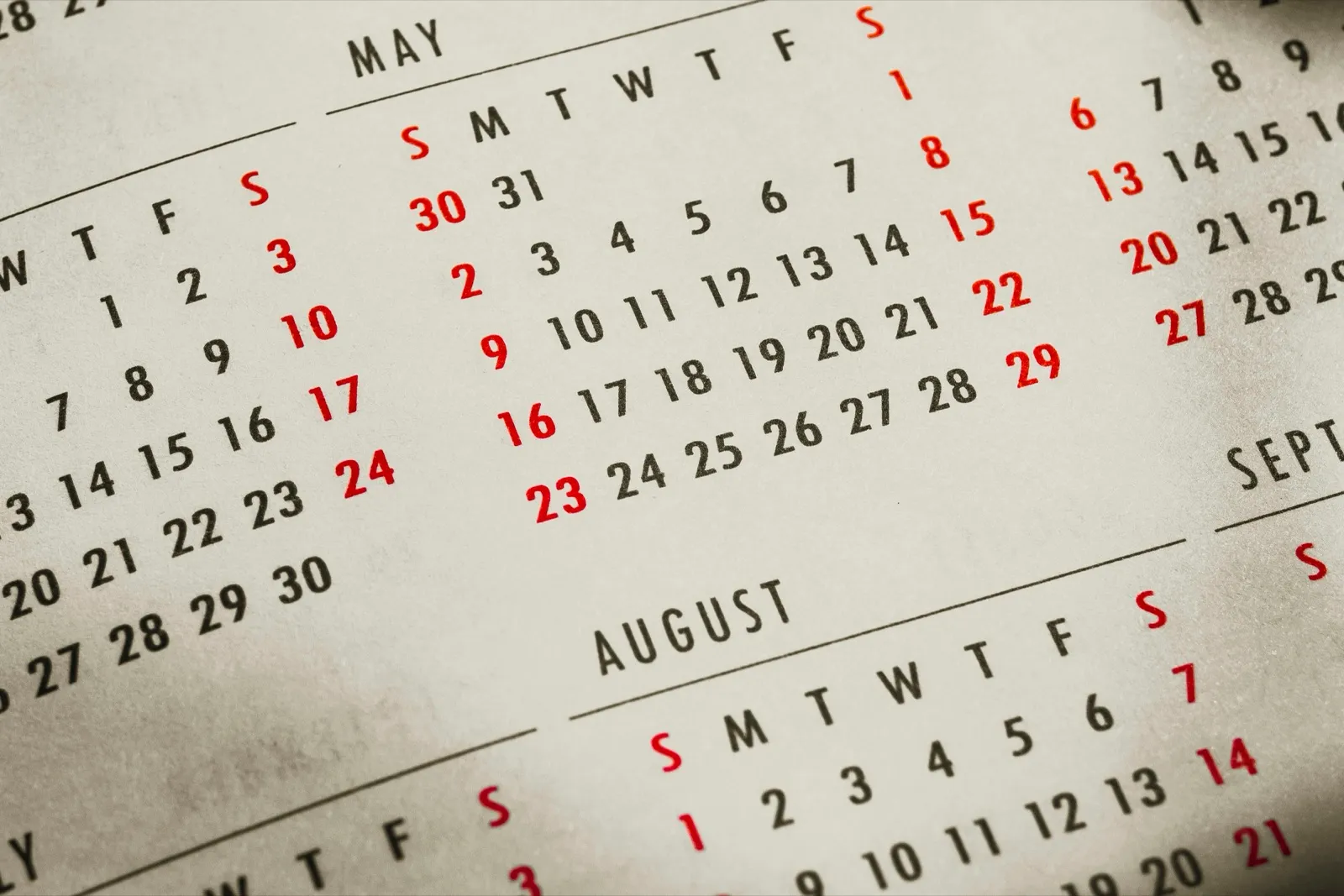 Close-up of a printed yearly calendar showing the months of May and August, with weekend dates in red