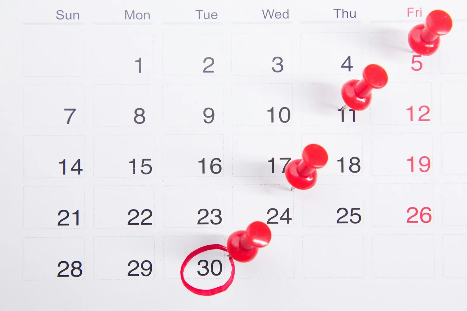 A white monthly calendar with red push pins marking appointment dates and one date circled in red