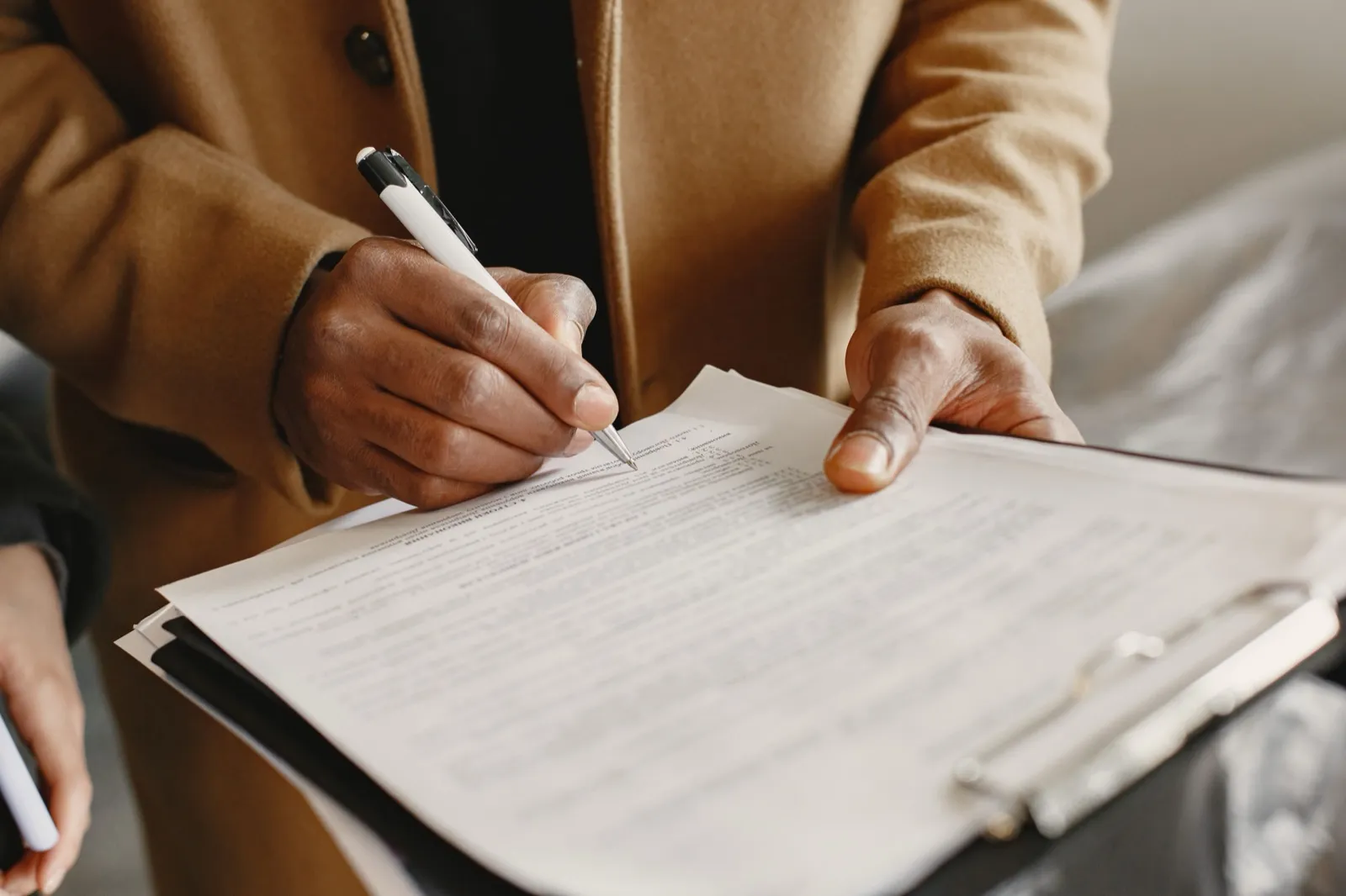 Close view of a person signing a printed form on a clipboard with a white pen