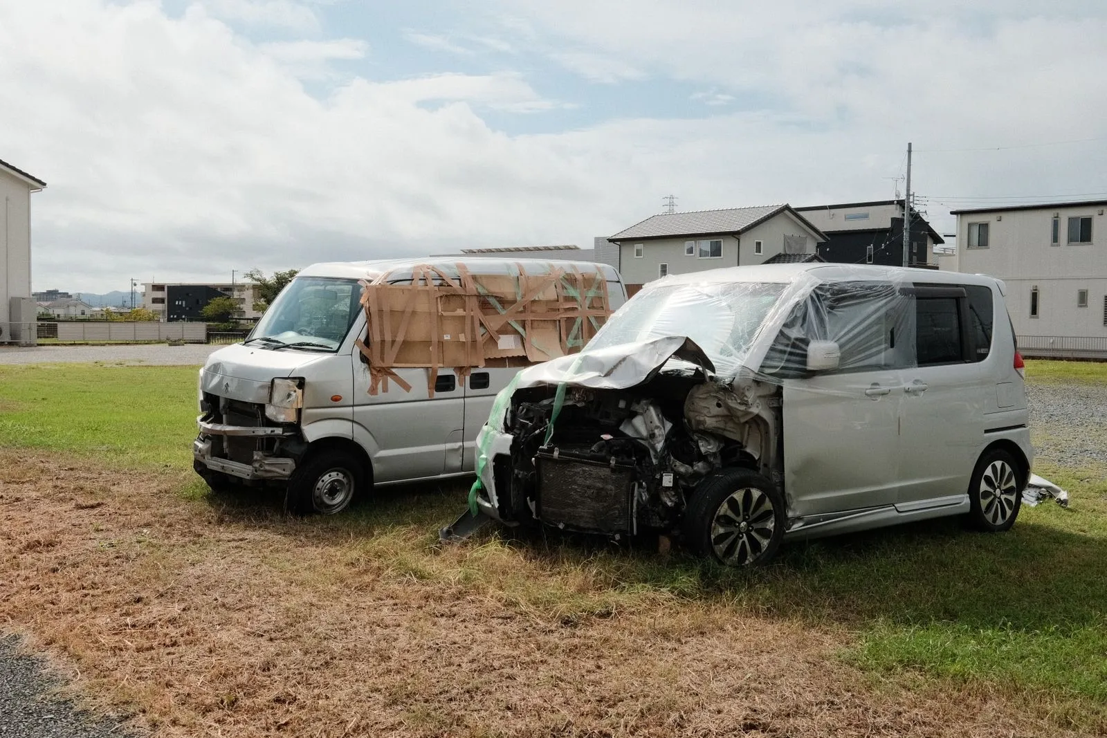 Two damaged passenger vans parked on a grassy lot after crashes, one with its front end crushed and its hood bent open