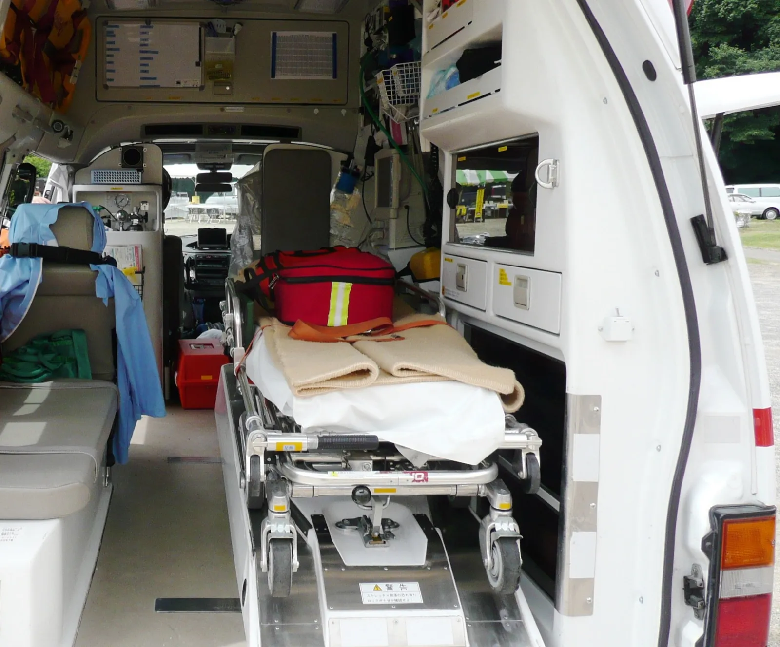 The open back of an ambulance showing a stretcher with a medical bag on it, a bench seat, and equipment cabinets