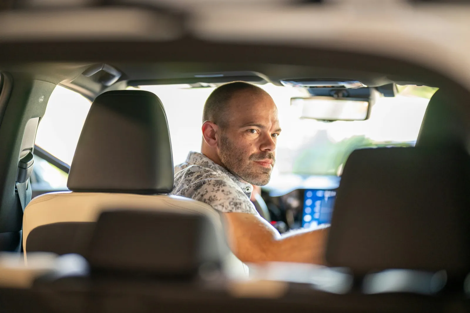 A driver turns in his seat to look back toward the rear of his car, seen between the back-seat headrests