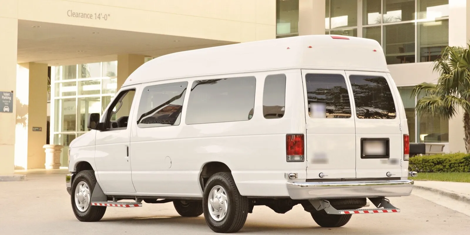 A white high-roof passenger van parked outside the covered entrance of a large building