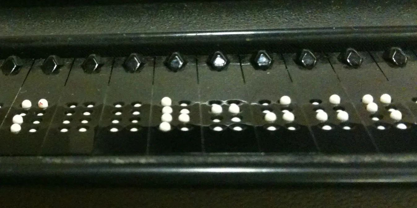 Close-up of a refreshable braille display, with raised white pins forming braille letters in a row of black cells