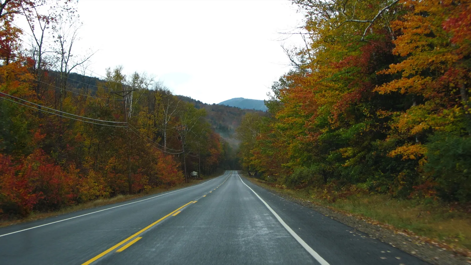The Kancamagus Highway near Lincoln in October, a two-lane road running between red, orange, and yellow trees toward a mountain