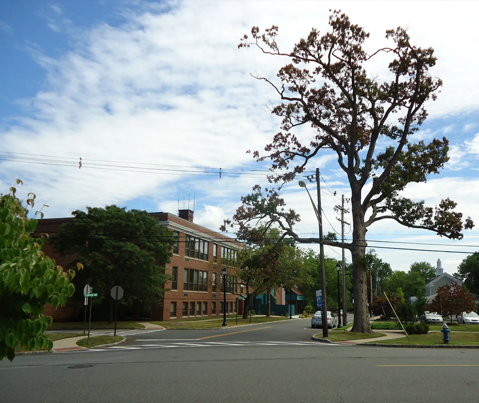 A brick municipal building on a tree-lined street corner in New Providence, New Jersey, under a partly cloudy summer sky