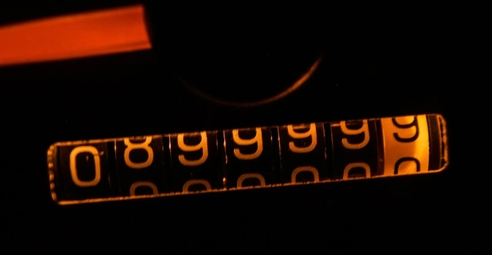 Close view of a lit mechanical car odometer with its digits rolling over