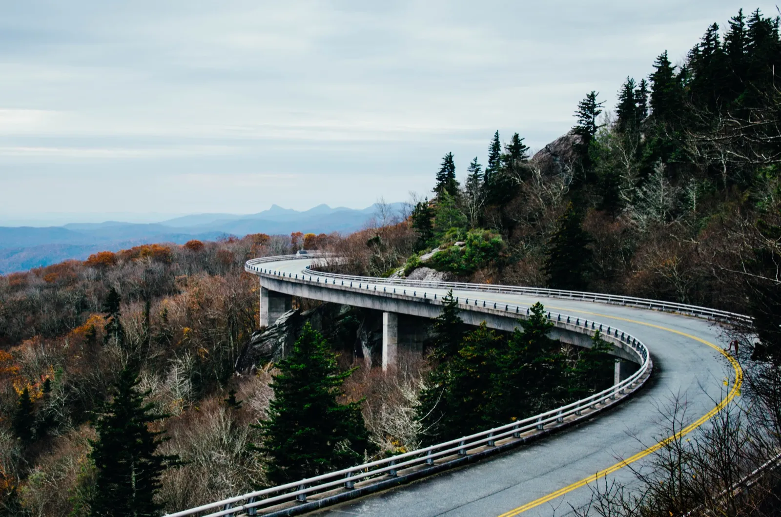 The Blue Ridge Parkway curving along the Linn Cove Viaduct near Linville, North Carolina, with late autumn trees and blue mountain ridges behind