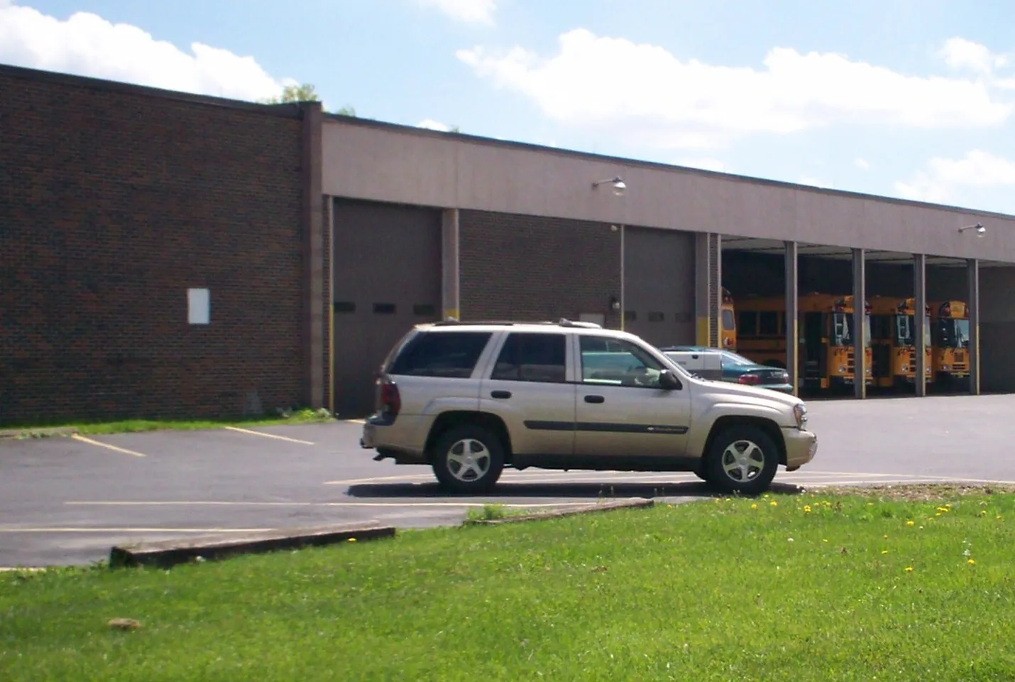 A school district bus garage in Kent, Ohio, with yellow school buses parked in its open bays and an SUV in the lot
