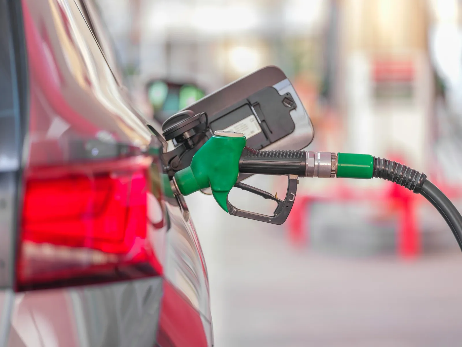 A green fuel nozzle in the open fuel door of a red car at a gas station