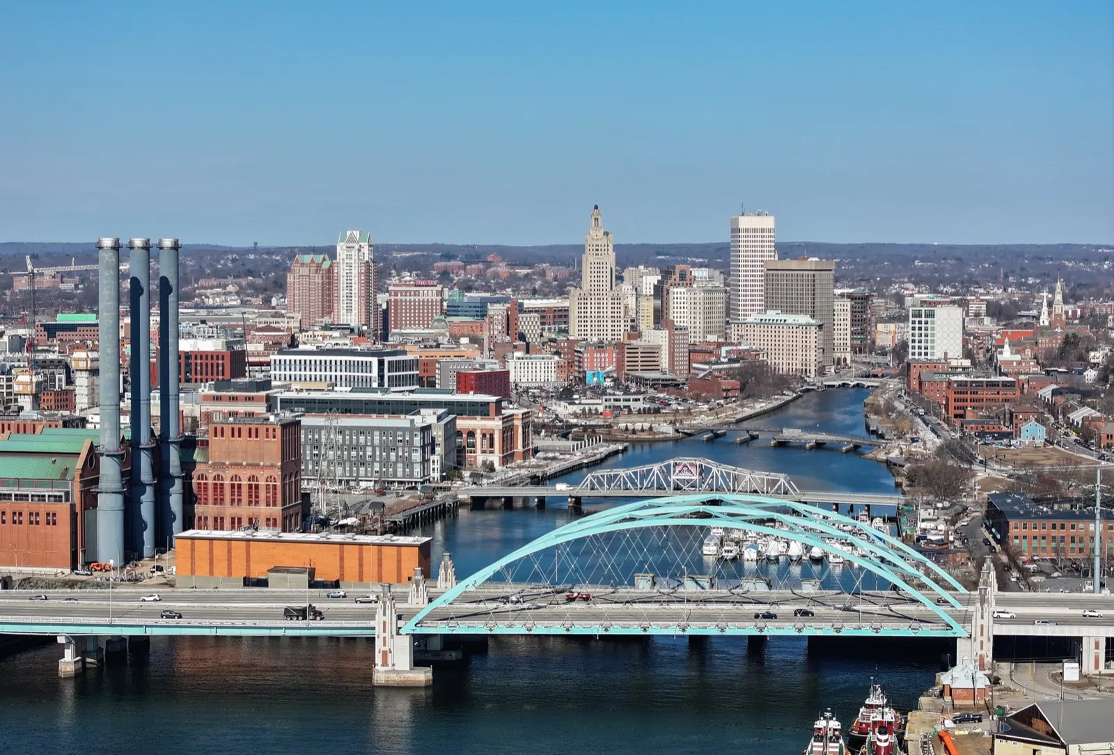Downtown Providence and the Providence River on a clear day, with a teal arch highway bridge in the foreground