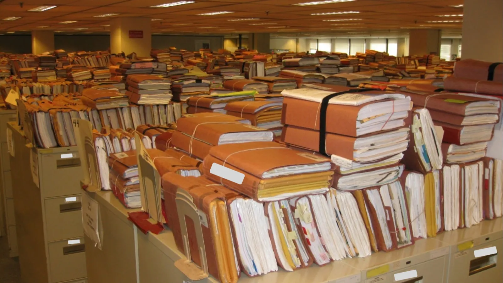 Bundled paper case files in brown folders stacked on rows of filing cabinets in a large office