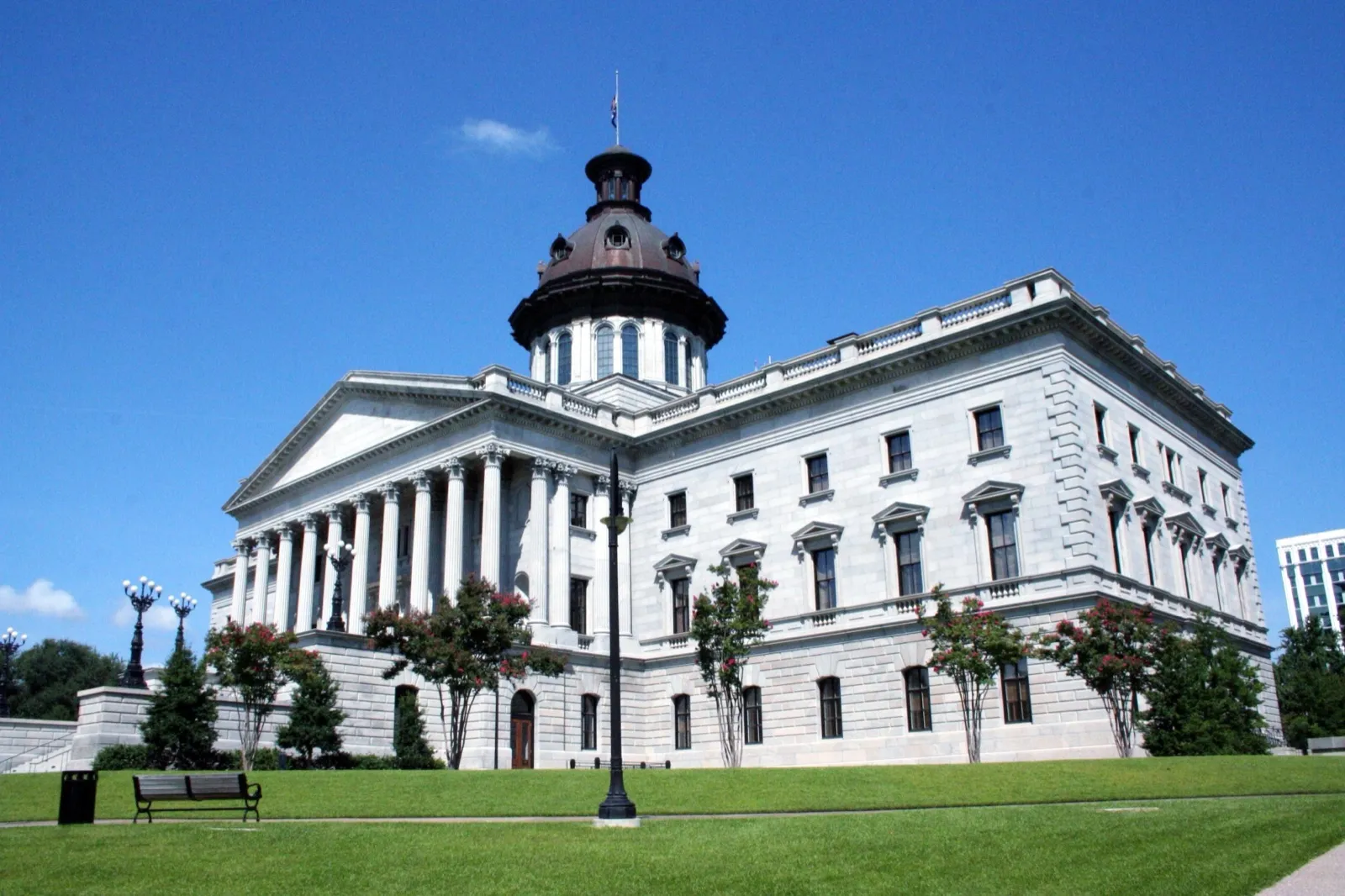 The South Carolina State House in Columbia, a gray granite building with a copper dome, seen across a green lawn under a blue sky