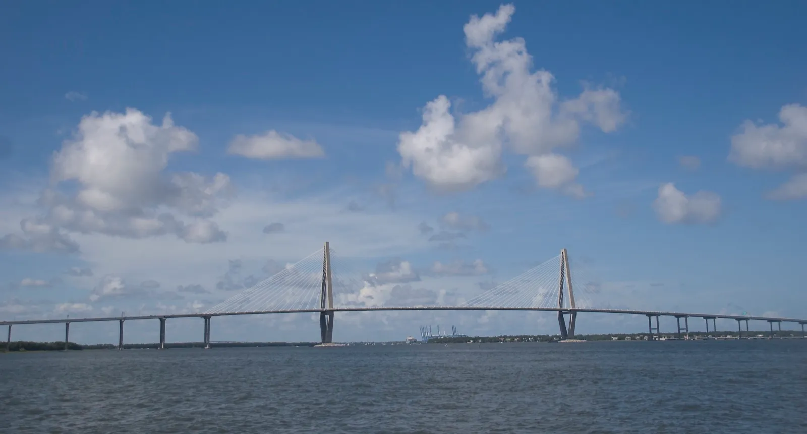 The Arthur Ravenel Jr. Bridge in Charleston, its two diamond-shaped towers and cables spanning the Cooper River under a blue sky with white clouds