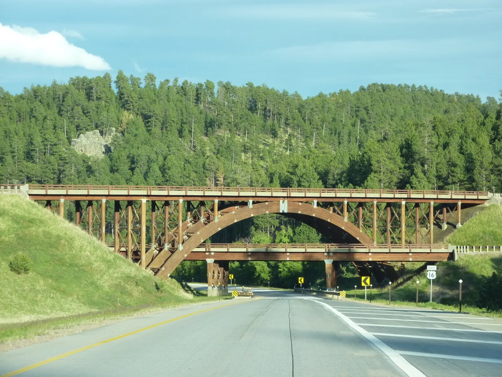 US Highway 16 at the Keystone Wye in the South Dakota Black Hills, passing under wooden arch bridges, with pine-covered hills behind