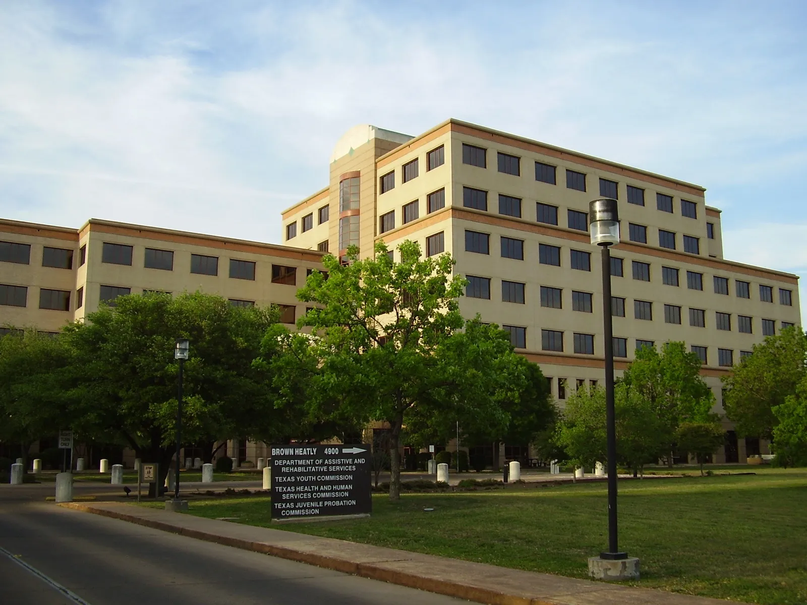 The Brown Heatly Building in Austin, a tan office building behind green trees, with a sign out front naming the Texas Health and Human Services Commission