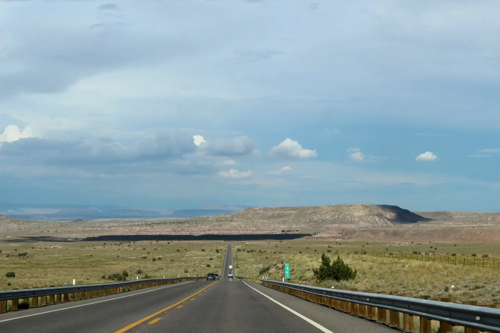 A two-lane highway running straight across open grassland on the Navajo Nation in Arizona, with mesas and a cloudy sky ahead
