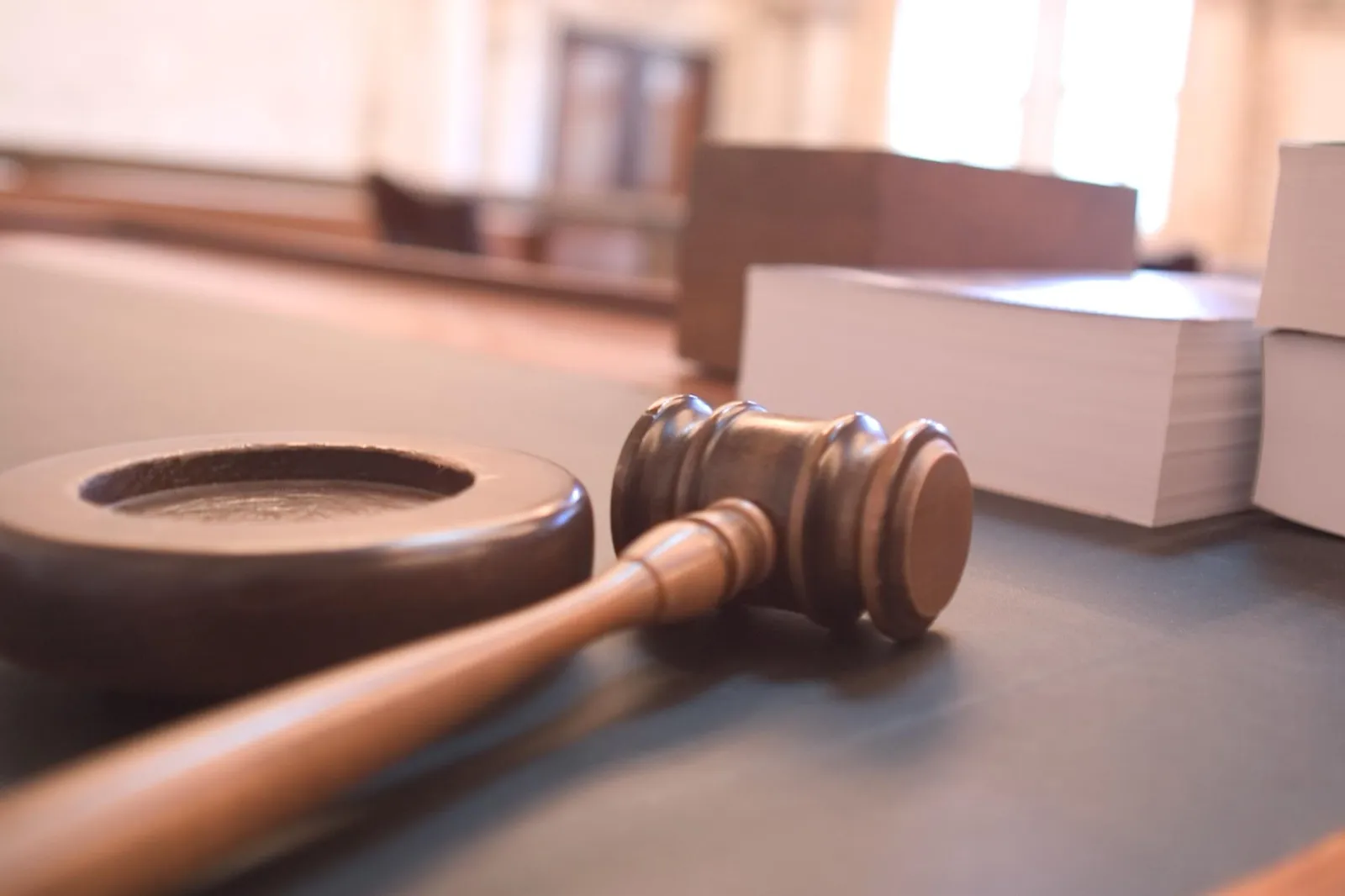 A wooden judge's gavel resting beside its sound block on a courtroom table, with stacks of thick books behind it