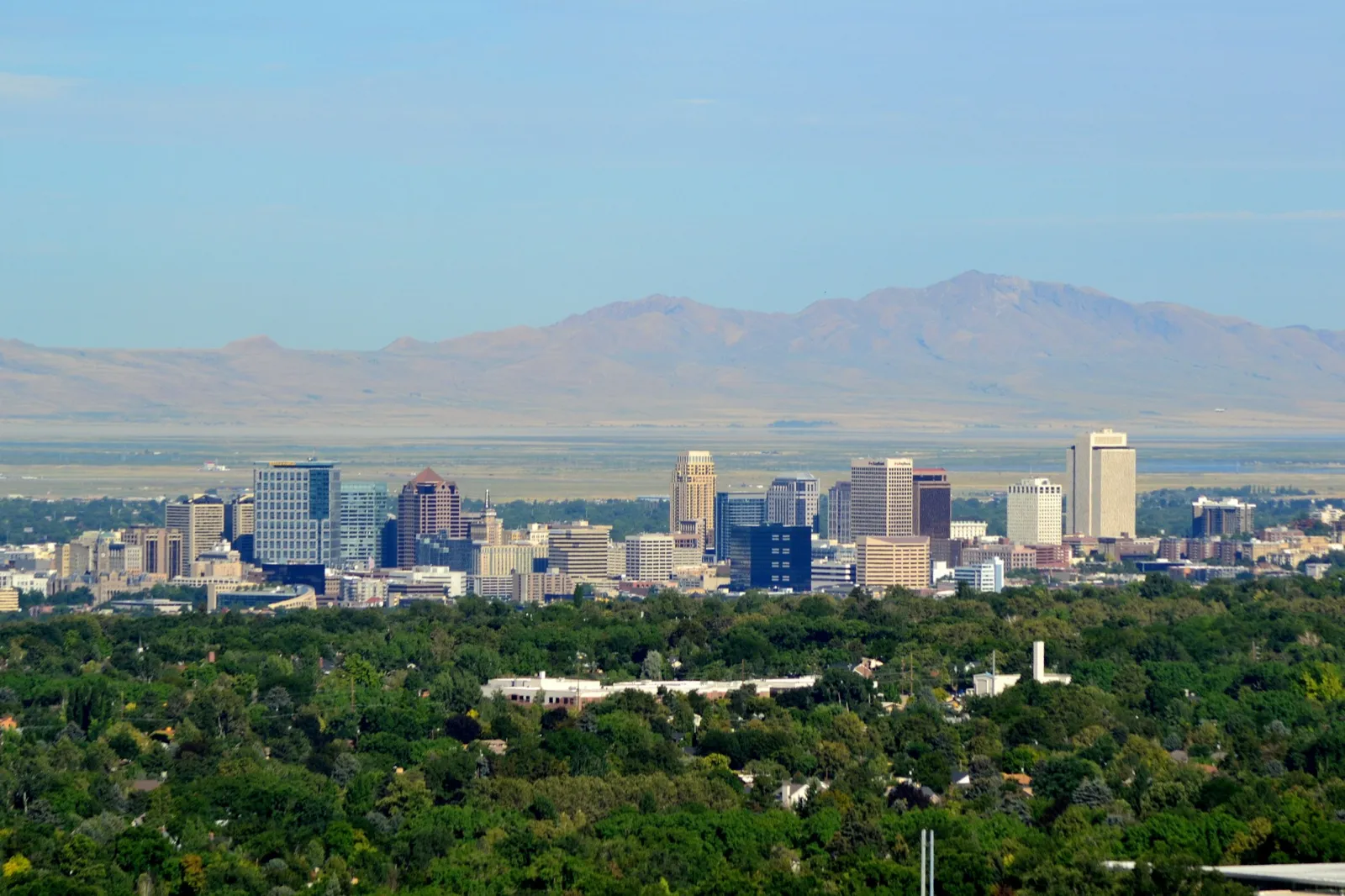 The Salt Lake City skyline seen from the east bench, with green trees in front and desert mountains beyond the city