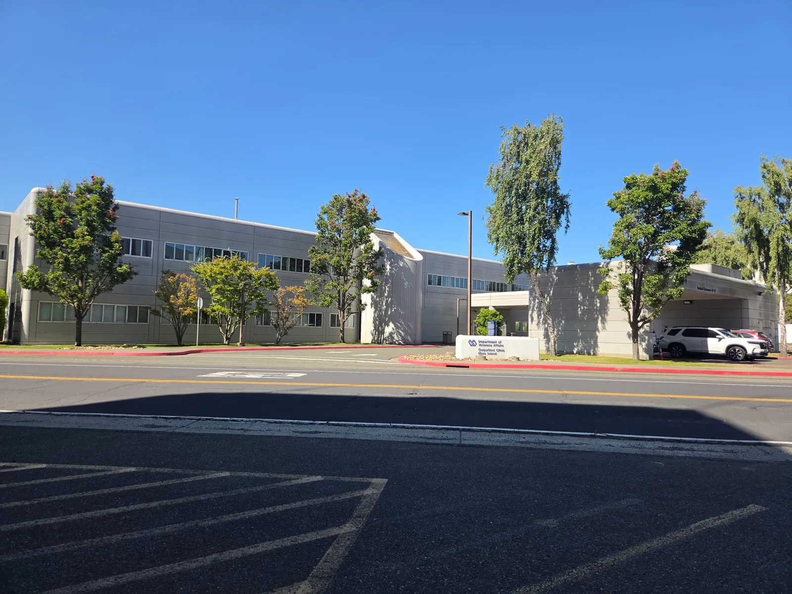 A two-story Department of Veterans Affairs outpatient clinic on a sunny day, with a covered drop-off lane at the entrance and trees along the street
