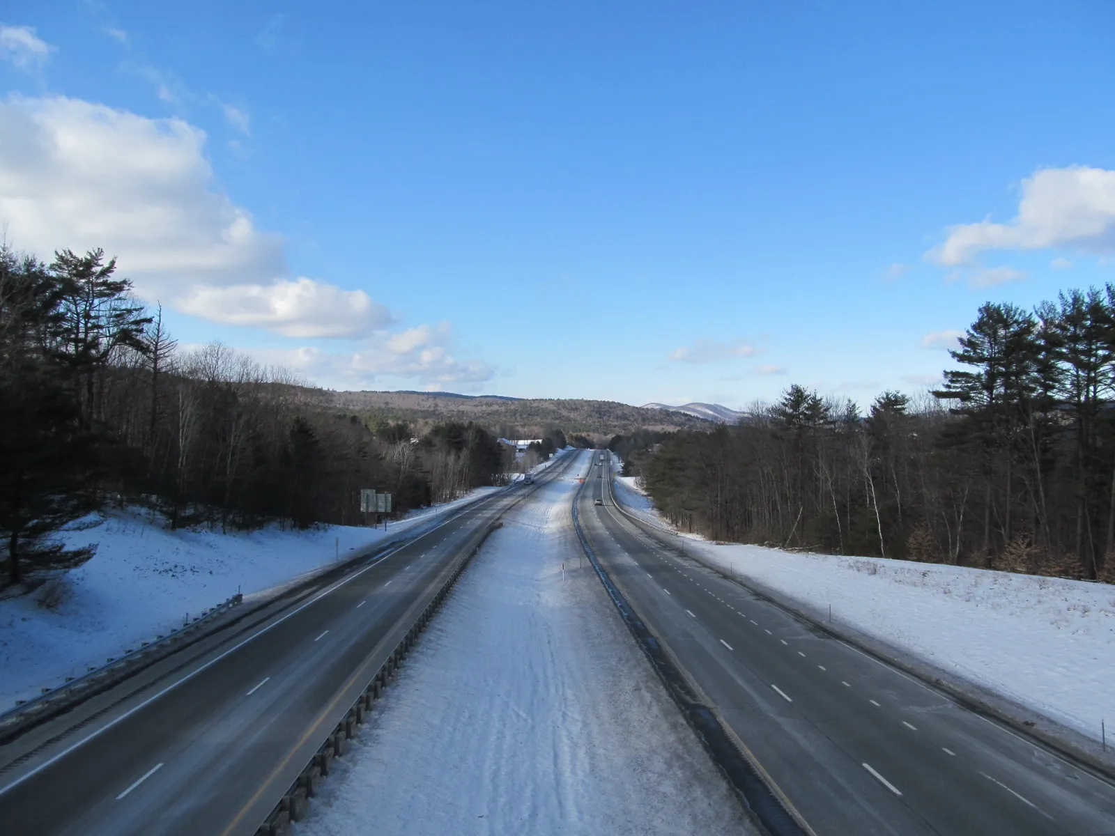 Interstate 89 running north through snowy woods near Hartford, Vermont, with hills on the horizon under a blue sky