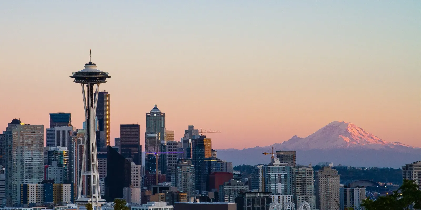 The Seattle skyline and the Space Needle at sunset, with Mount Rainier glowing pink in the distance