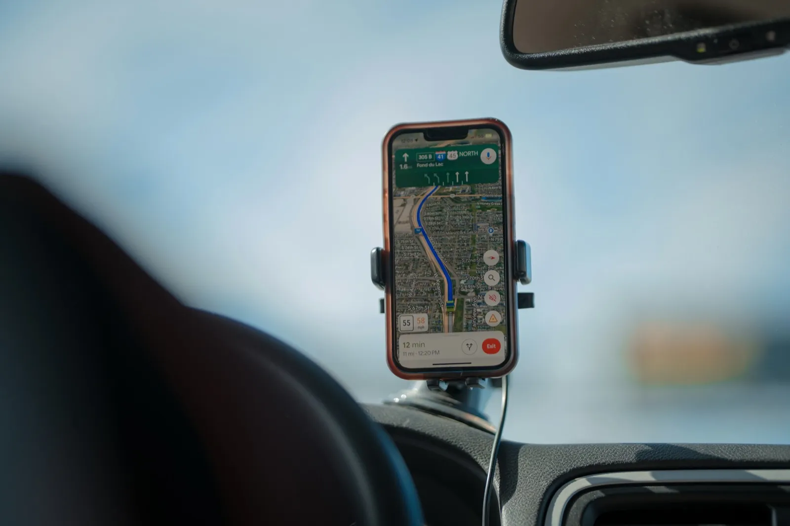 A smartphone in a windshield mount showing a highway route on a map, seen from the driver seat