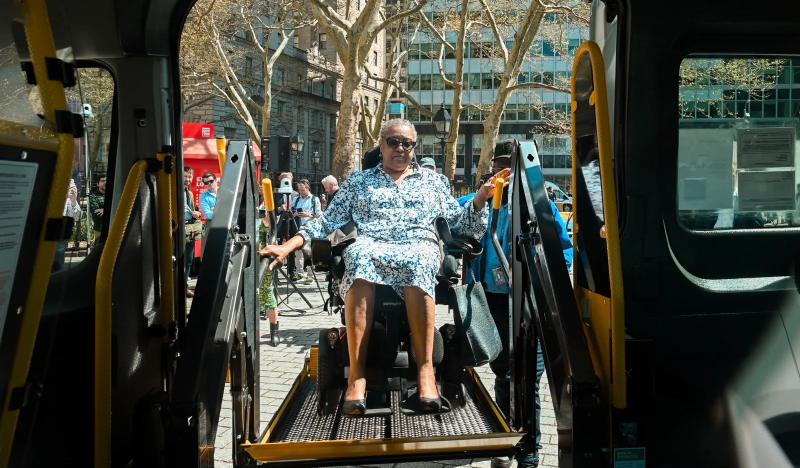 A woman in a power wheelchair rides a lift up into a wheelchair van, seen from inside the van between the lift arms