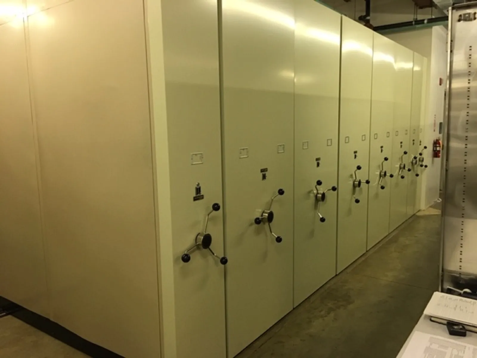 A row of tall beige rolling archive shelves with crank handles in a government records room